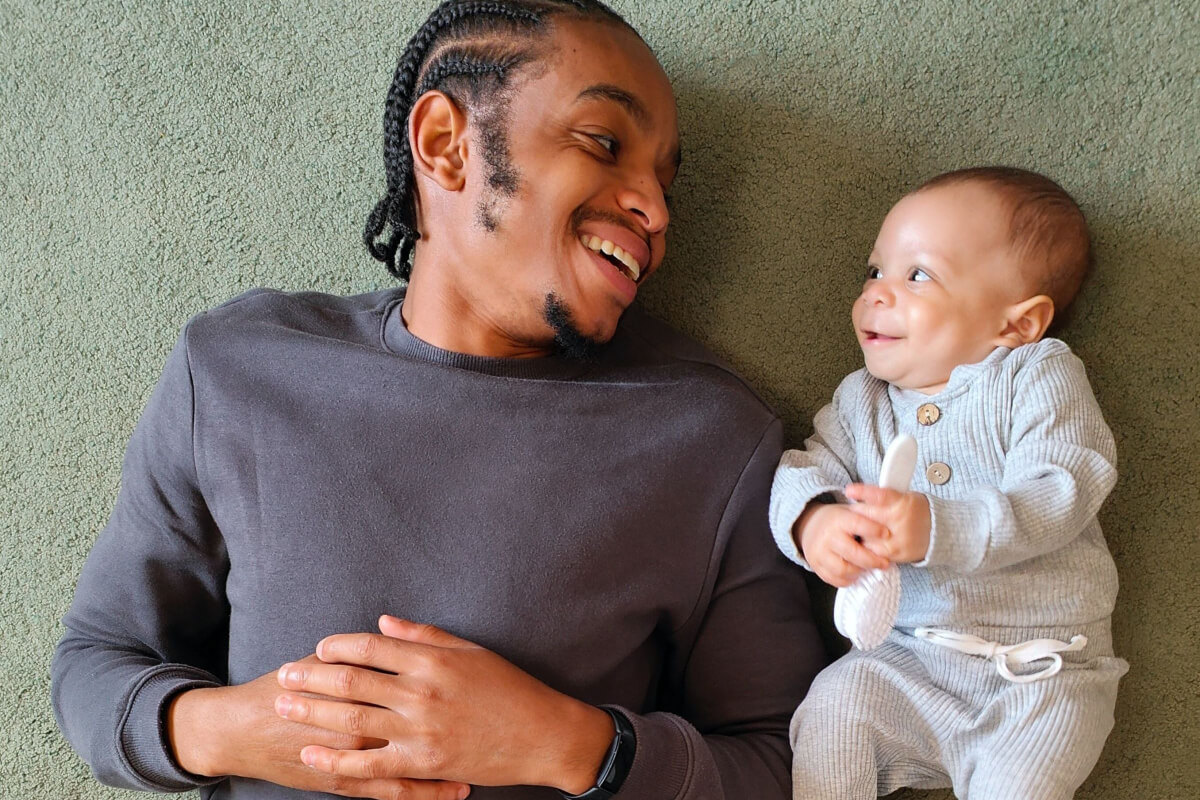 black father with baby lying together looking at each other showing how they can smile and be happy connecting