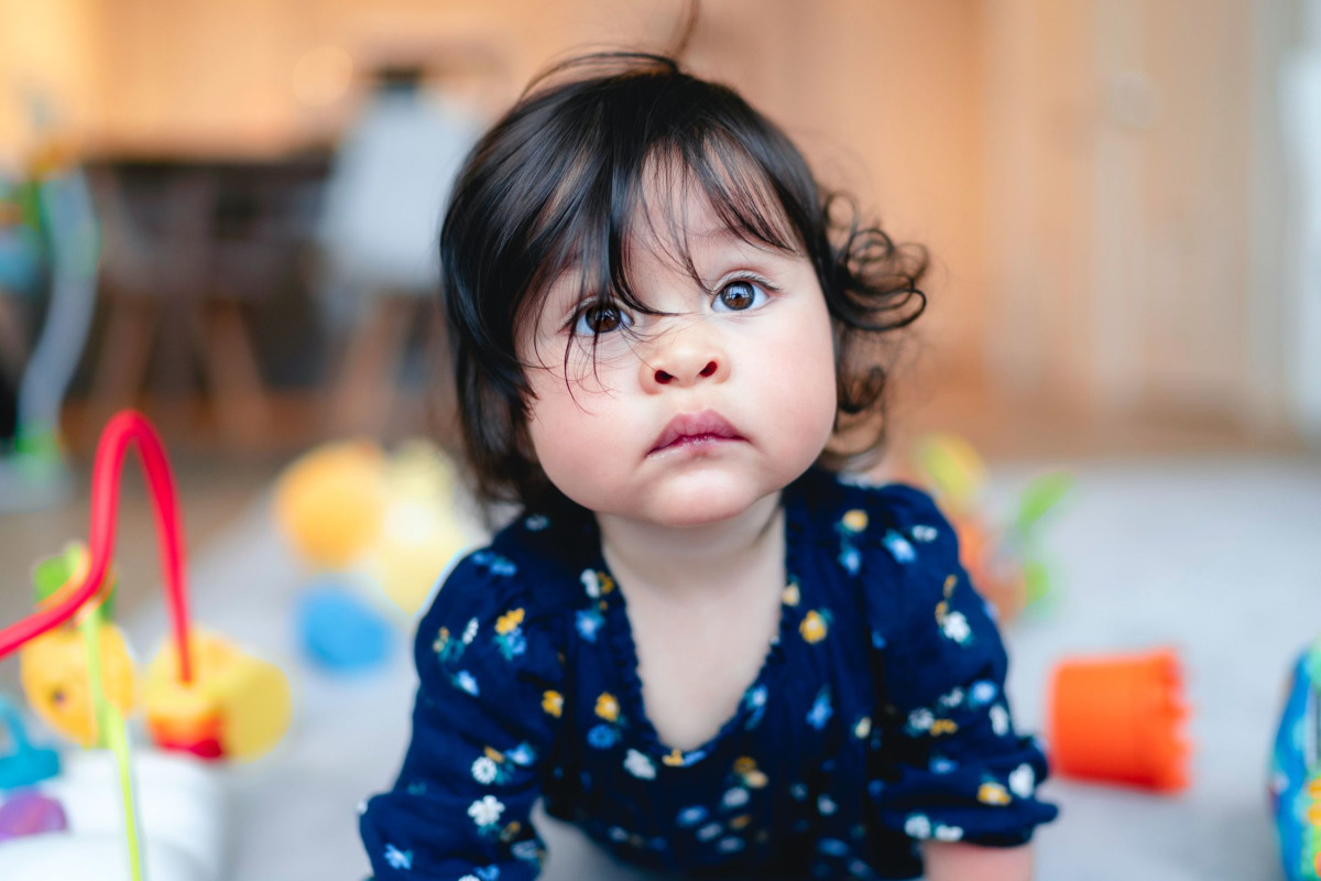 female toddler with dark hair falling in her eyes as she looks up with puzzlement in her eyes
