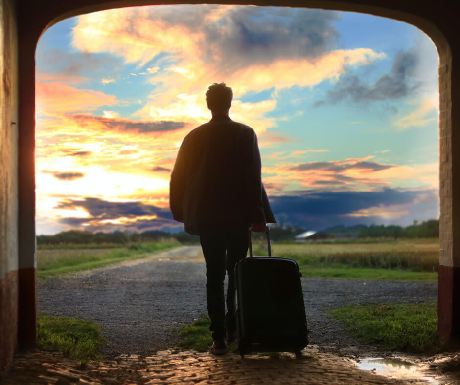 silhouette of male standing away from the viewer and looking into sunset with suitcase in hand on a journey towards greater emotional fitness