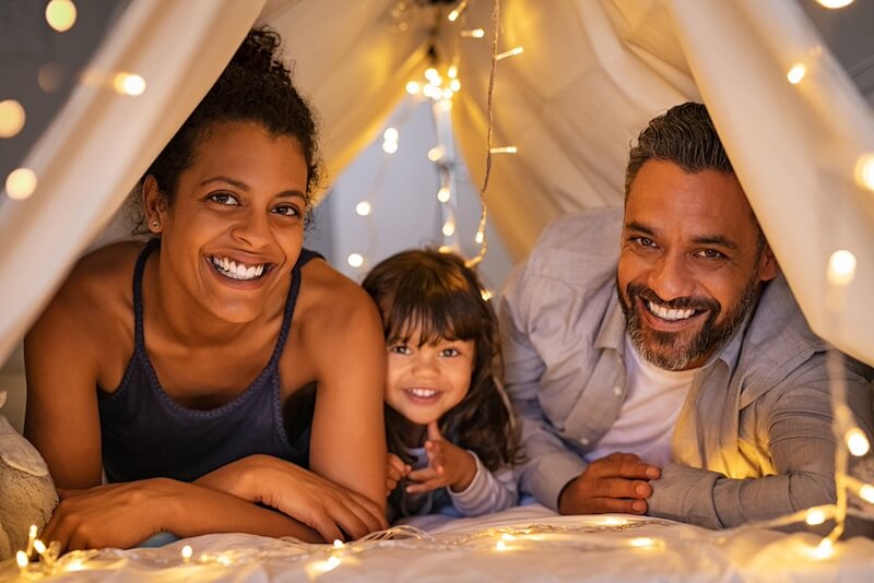hispanic mom, dad and daughter under pretty lighted tent all smiling enjoying the family moment
