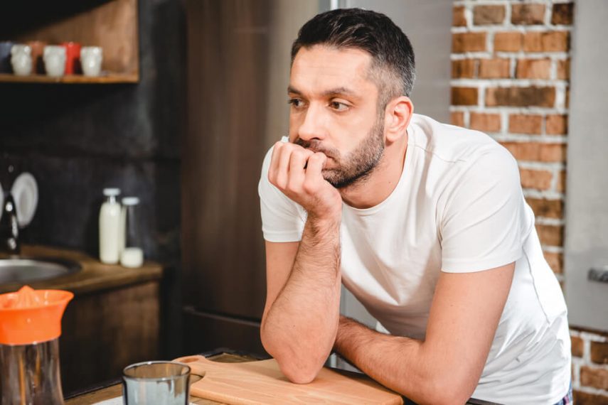 male leaning against counter with his fist supporting his chin and with a sad, forlorn look on his face