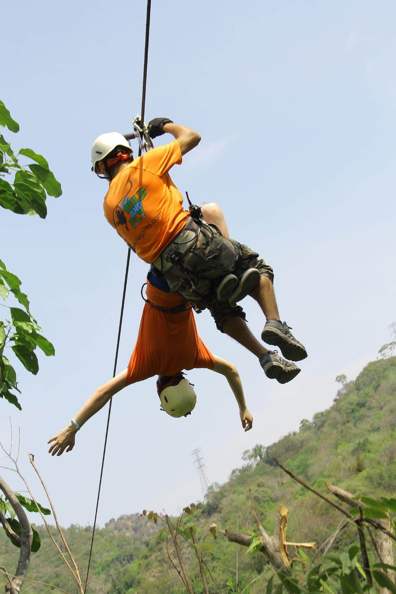 two people on a zip line with one hanging upside down in mid-air