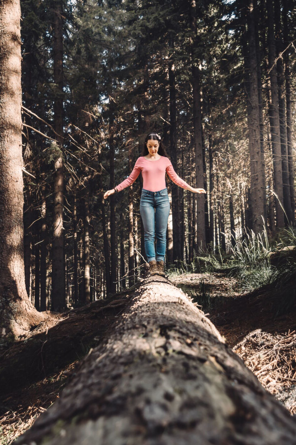 young white woman gingerly walking on a log in the middle of a forest