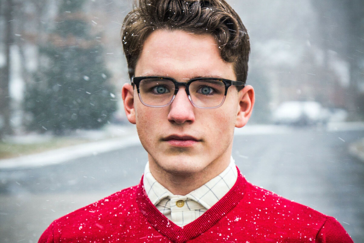young white guy staring right through the viewer wearing red sweater over shirt with a snowy backdrop